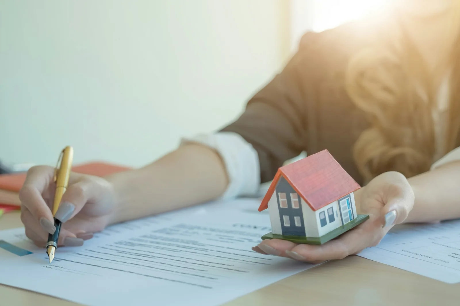 Person signing rebate paperwork while holding a small model house