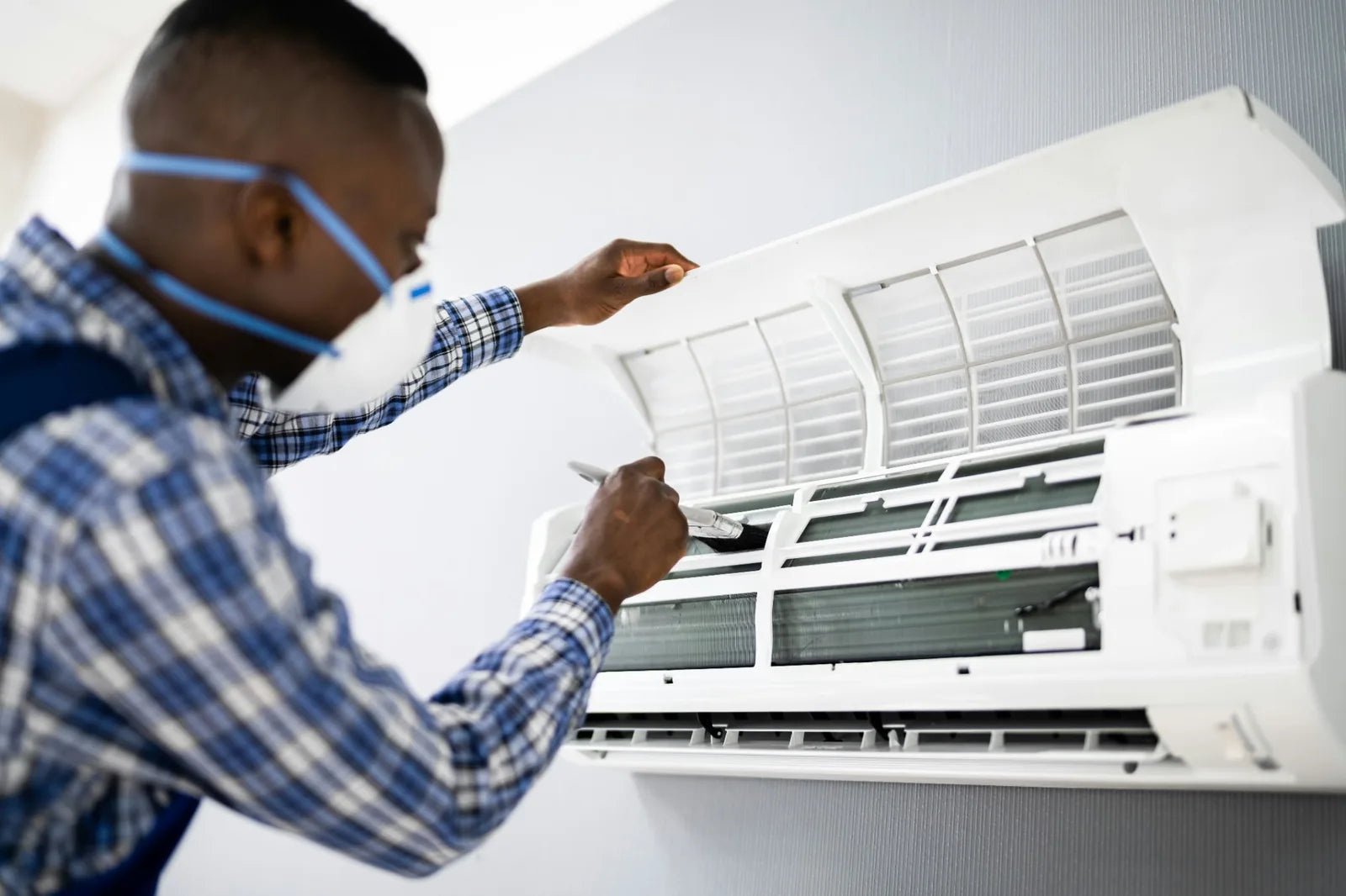 Person in a dust mask opening a wall-mounted mini-split to clean the filter