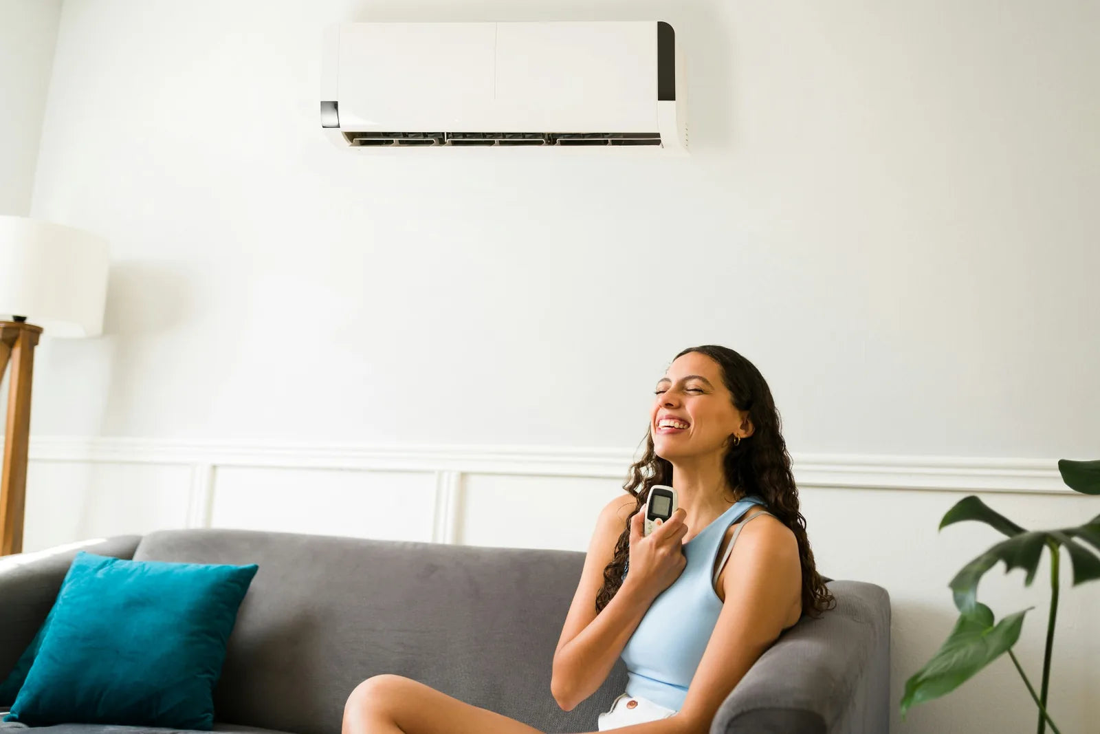 Woman relaxing on a sofa using a remote under a wall-mounted mini-split heat pump